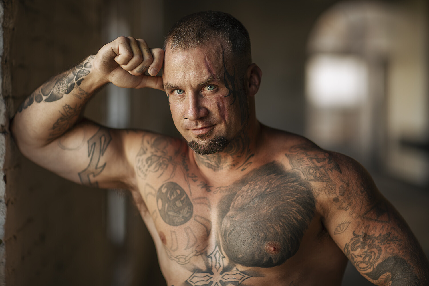 Shirtless man with extensive tattoos posing in industrial interior space