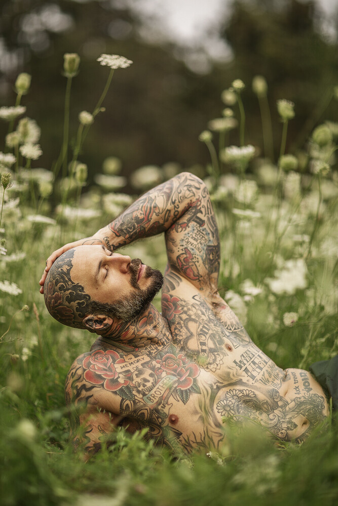 Heavily tattooed man with head tilted back among wildflowers in a field