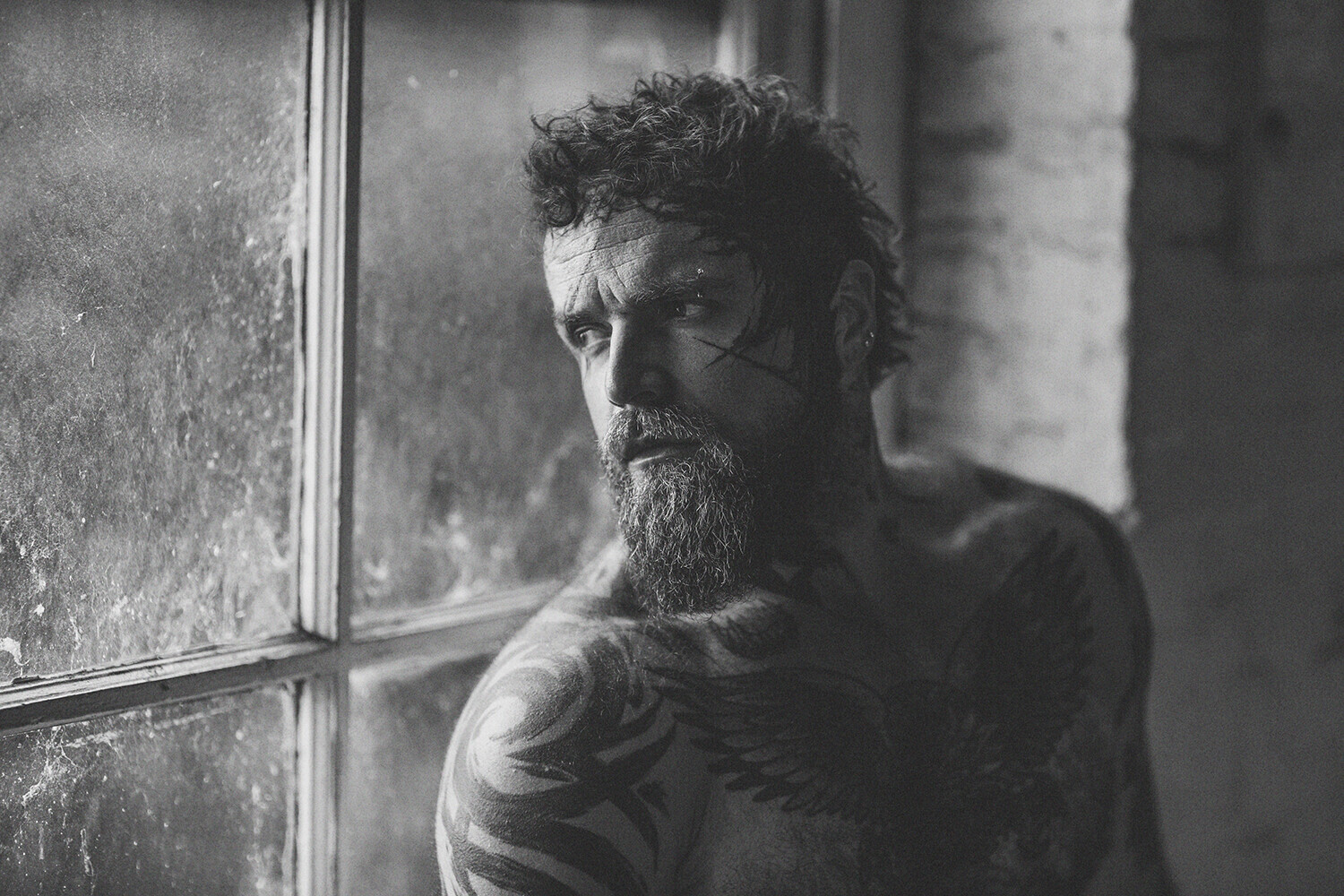 Bearded man with dark hair gazes toward a window with geometric panes in black and white portrait