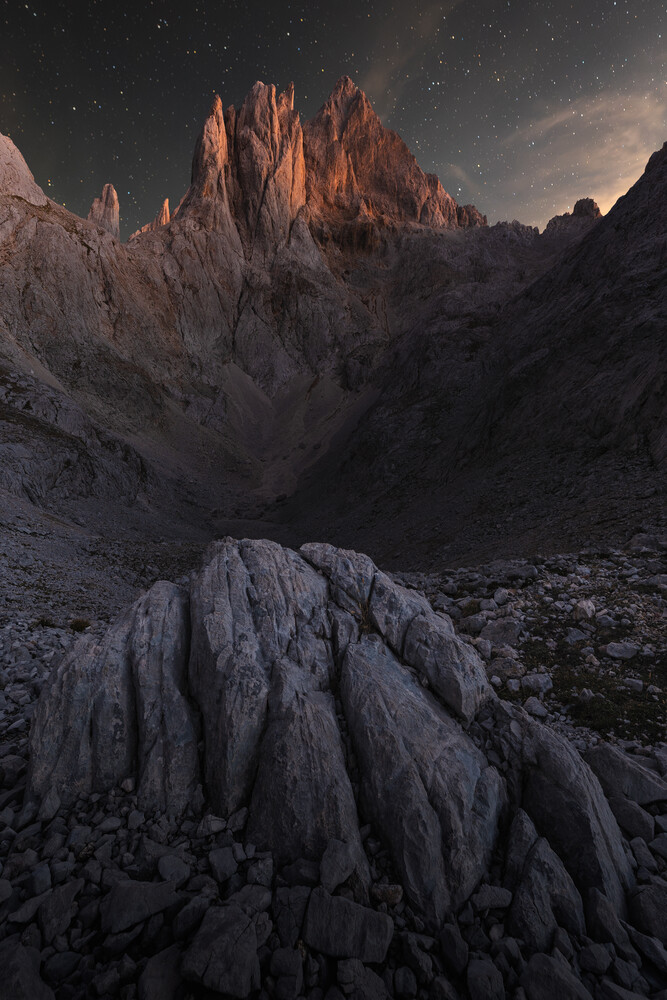 Snow-covered rocky peaks illuminated by alpenglow at dusk in a dramatic mountain landscape