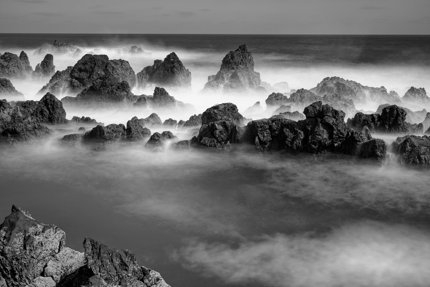 Rocky coastline shrouded in mist with jagged stones emerging from smooth, flowing water