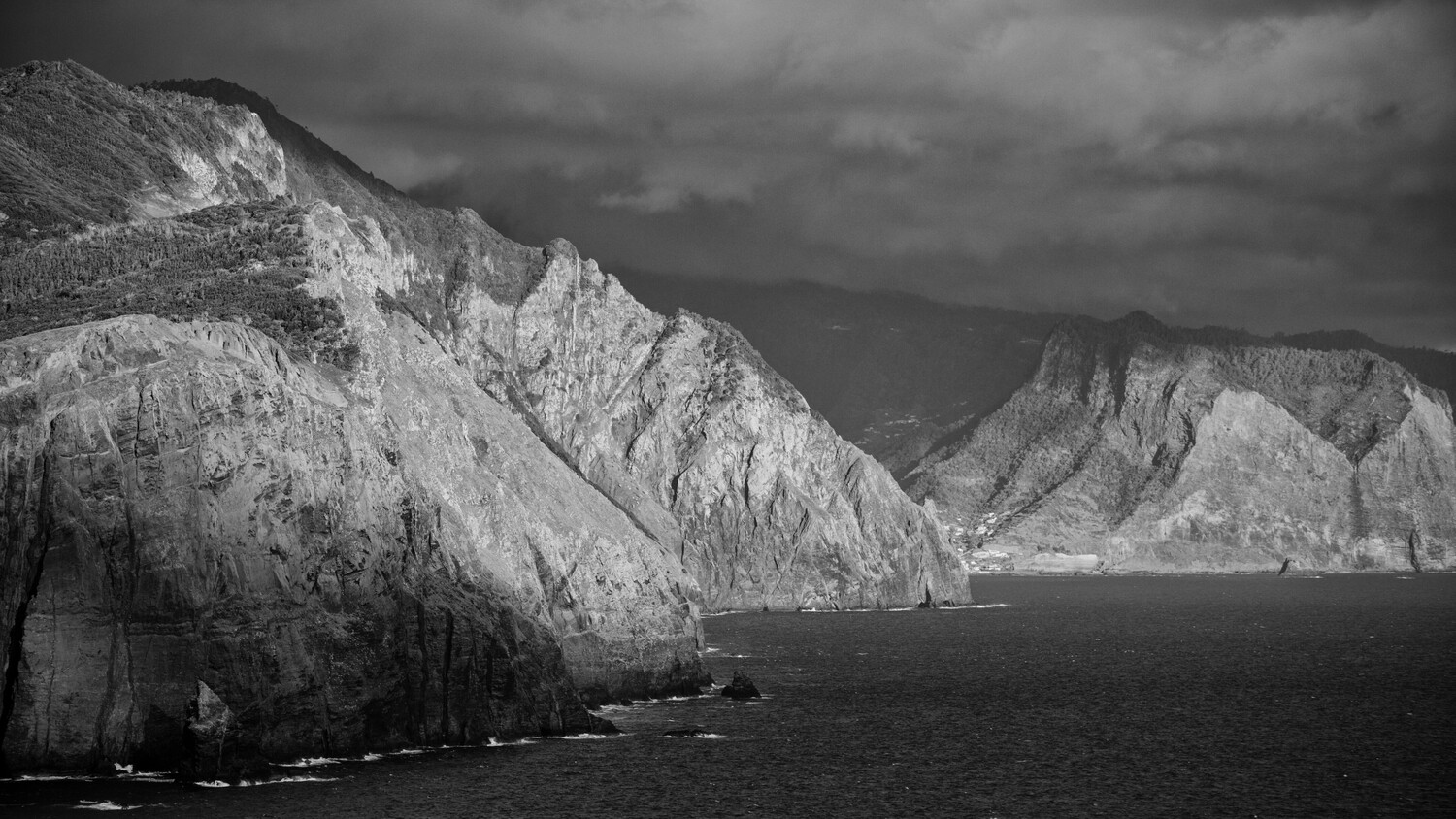 Dramatic white chalk cliffs rise steeply from dark ocean waters under stormy sky