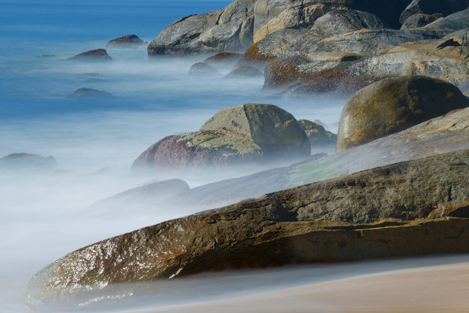 Misty seascape with smooth waves and moss-covered rocks using long exposure
