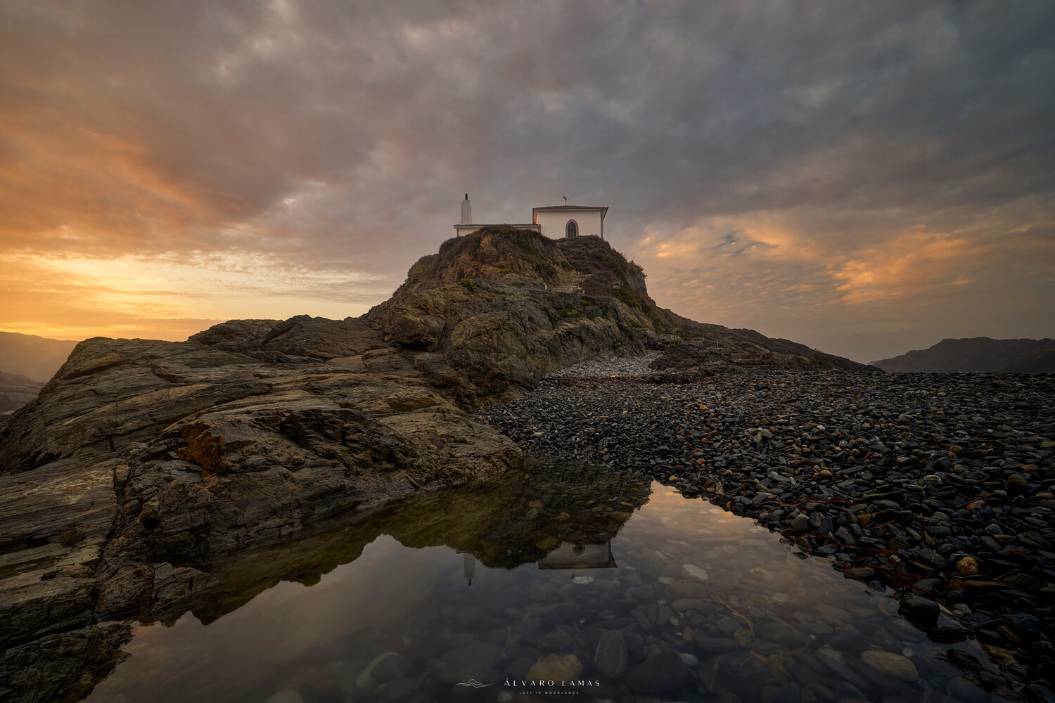 Coastal landscape with stone structure on rocky hilltop at sunset, reflected in tidal pool