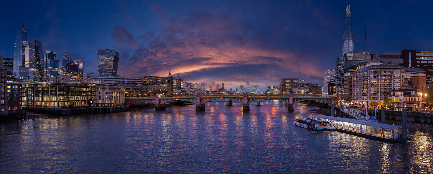 London skyline at dusk with illuminated buildings reflected in the Thames and a passenger boat in the foreground
