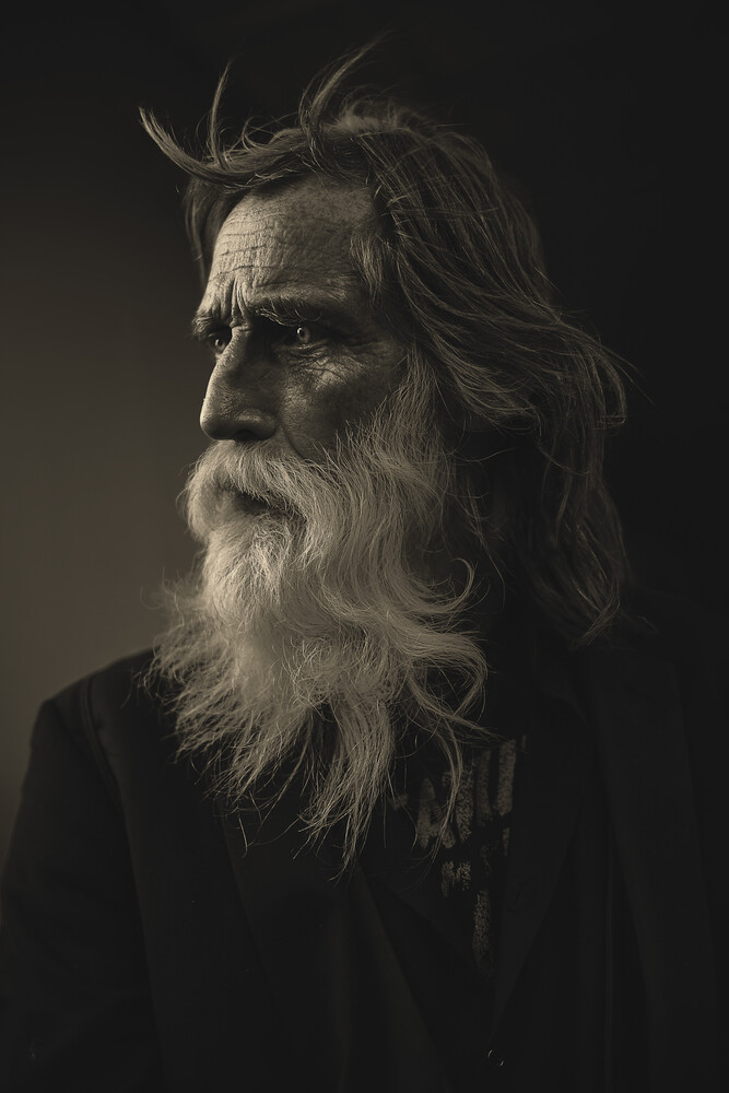 Elderly man with long white beard and hair in three-quarter profile against dark background