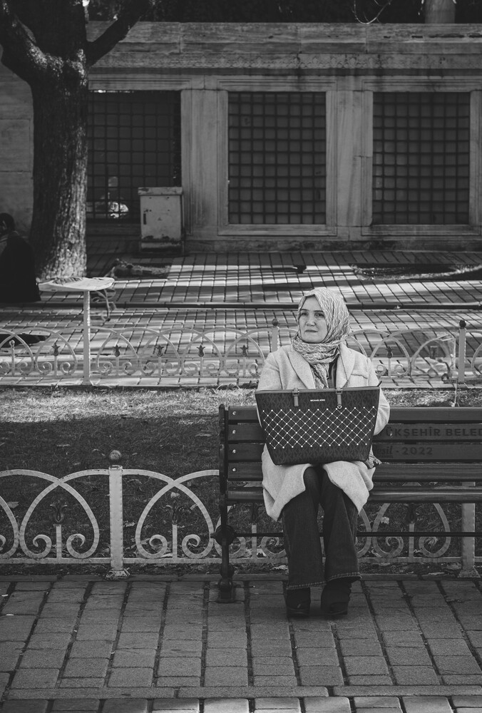 Elderly woman holding laptop seated on bench in urban setting, black and white
