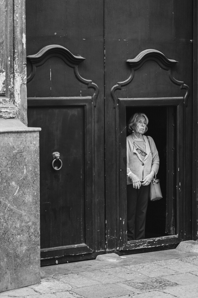 Woman standing in doorway of dark wooden double doors with ornate handles