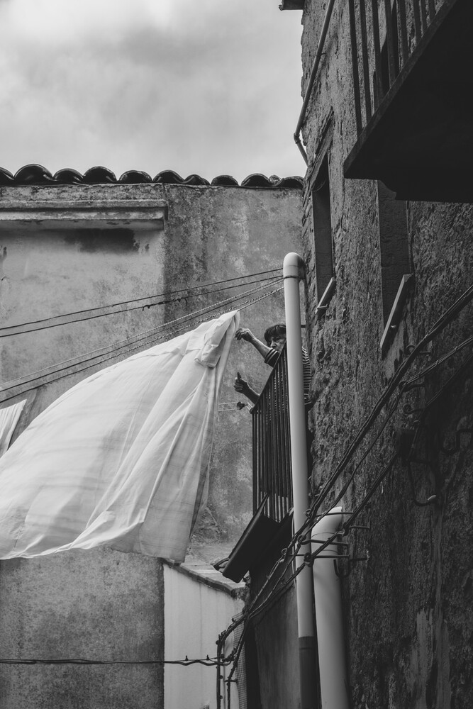 Billowing white fabric suspended from a weathered stone structure overlooking a still water body