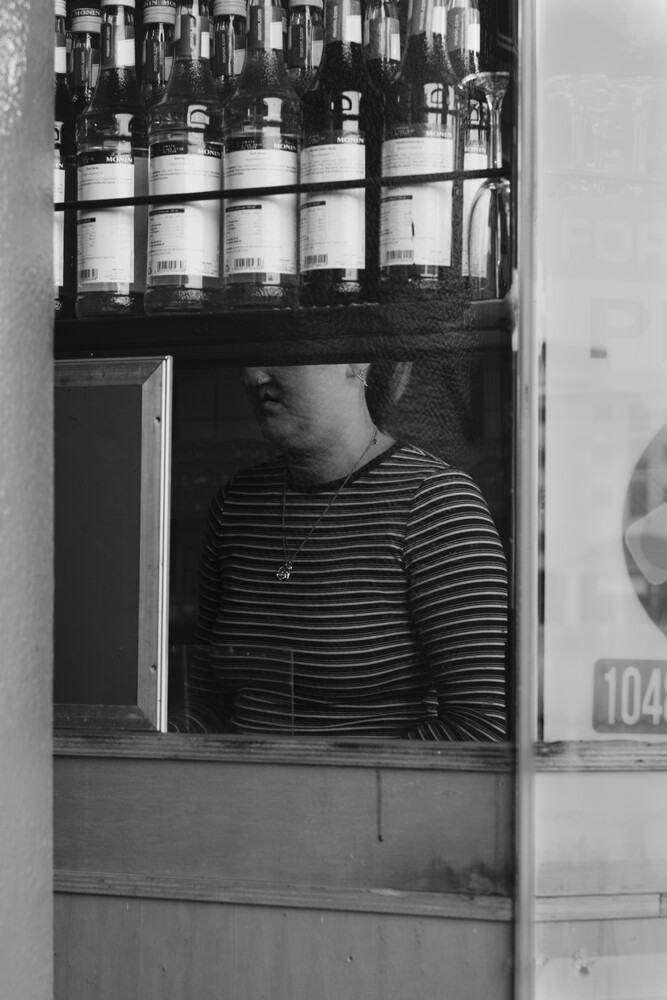 Person in striped shirt viewed through storefront window with product bottles displayed above