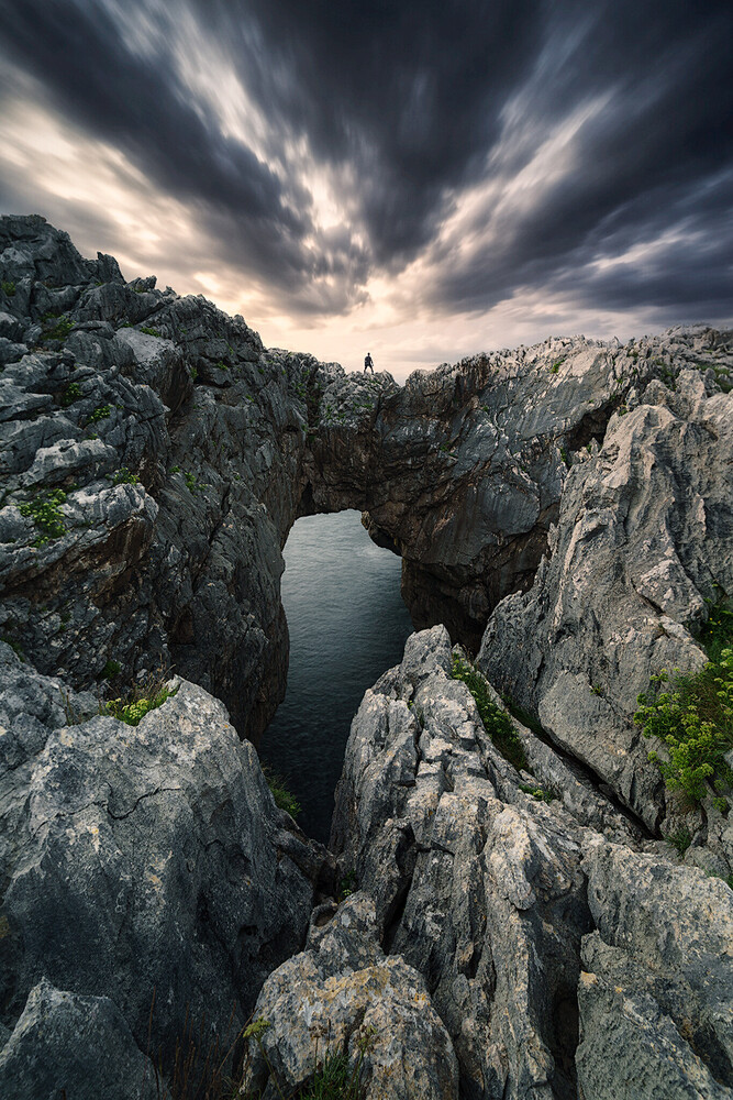 Rocky coastal arch framing calm water beneath dramatic storm clouds