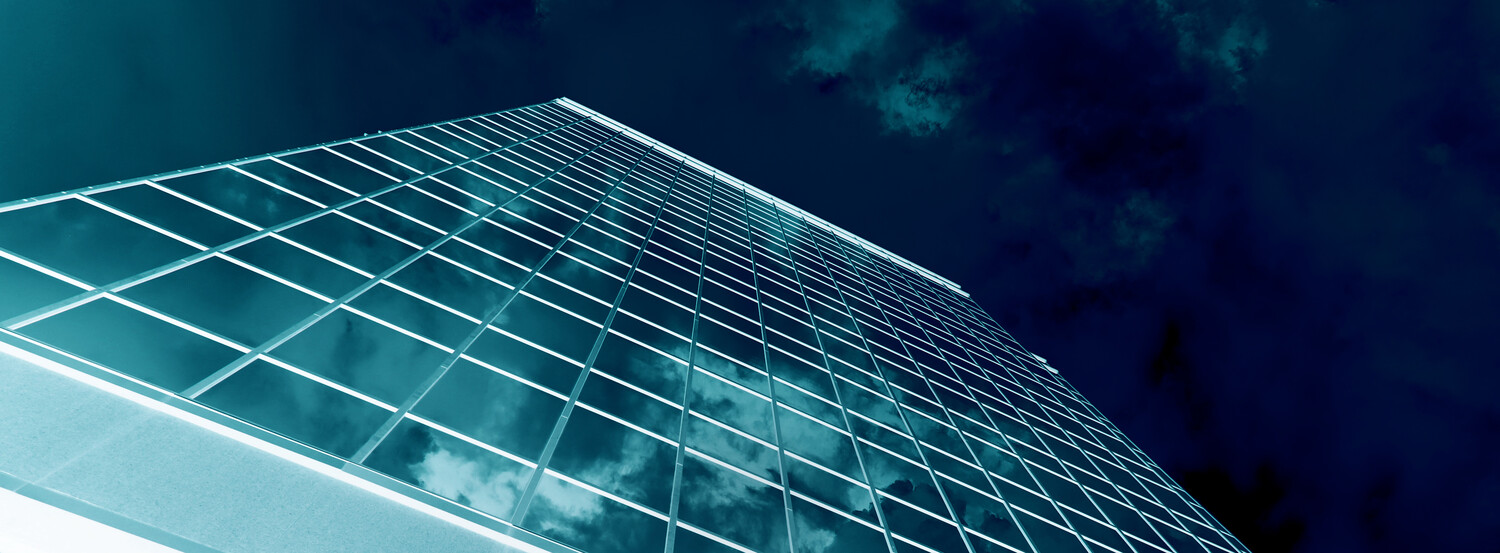 Modern glass and steel skyscraper facade photographed from low angle against dark sky