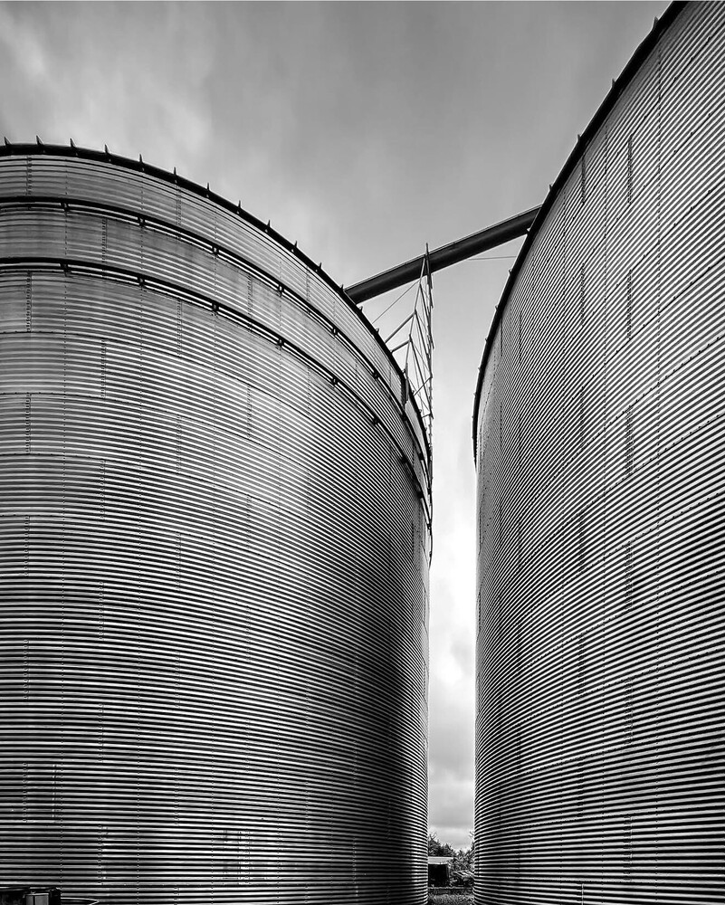 Two large cylindrical grain storage silos in black and white with geometric metal ribbing patterns