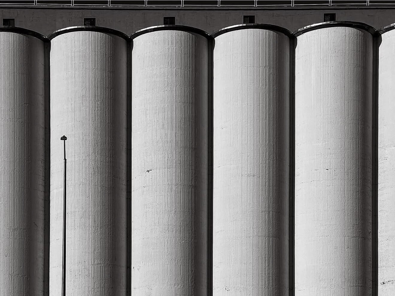Five tall cylindrical concrete or metal silos with vertical ribbed texture against dark sky