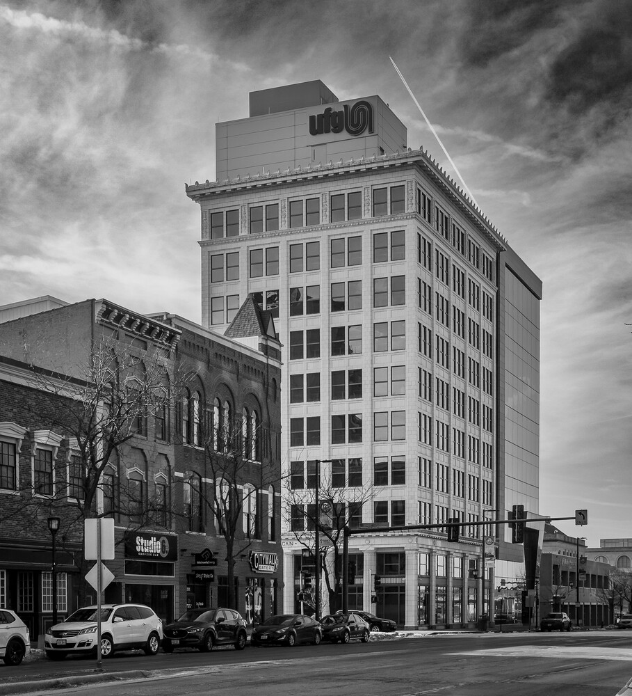 Black and white urban street scene with multi-story buildings and dramatic cloudy sky