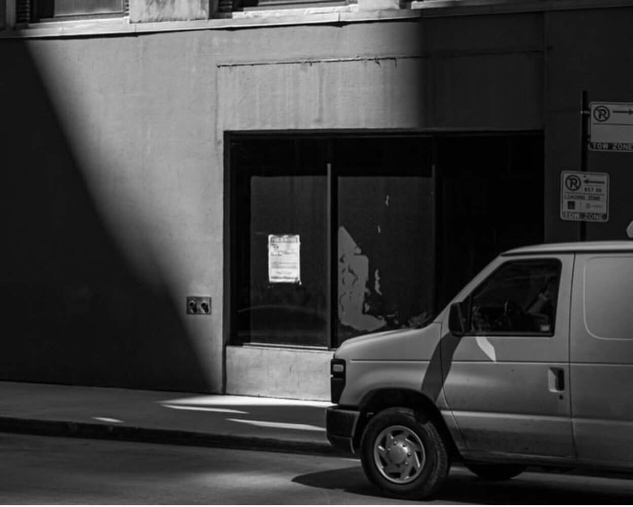 Van parked beside darkened storefront with closed black doors in black and white street photography