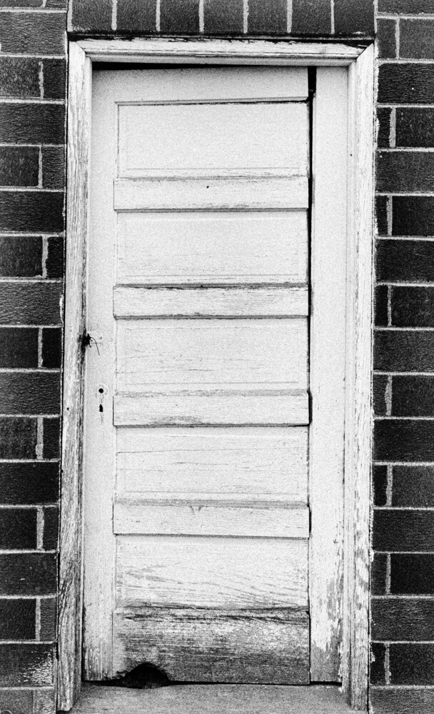 Weathered white wooden door with horizontal panels set in dark brick wall
