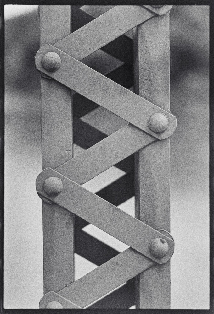 Black and white photograph of interlocking metal bands with spherical rivets creating a twisted geometric pattern