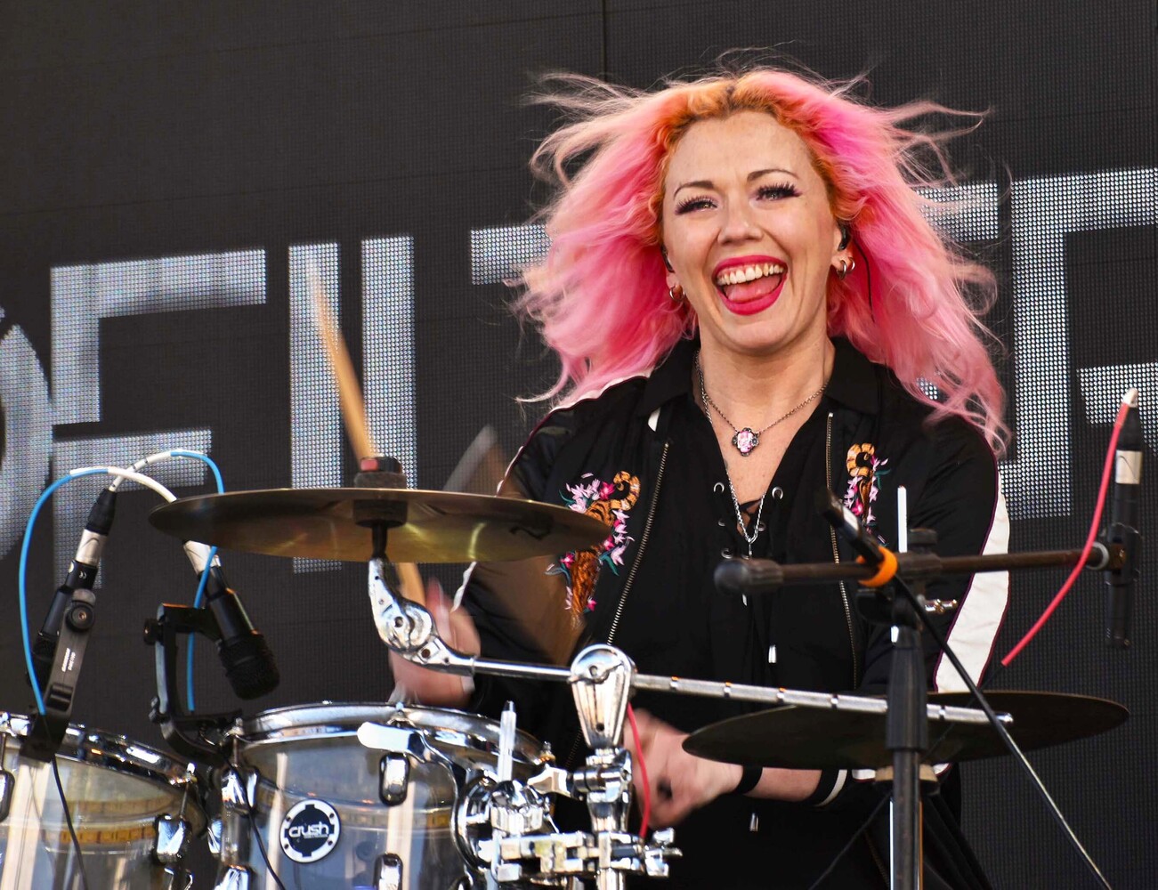 Drummer with bright pink hair performing at live event with professional drum kit