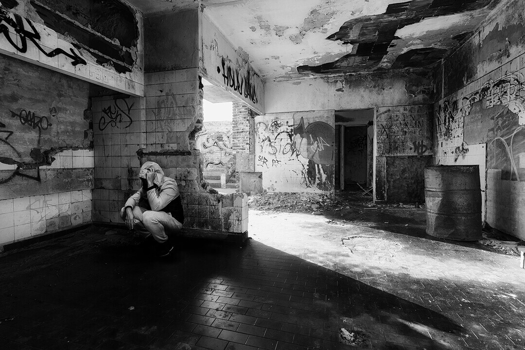 Solitary figure crouching in deteriorating interior space with dramatic side lighting