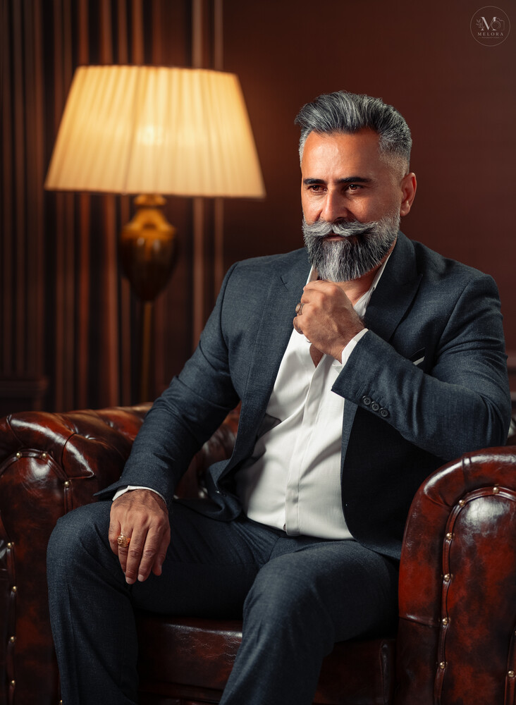 Bearded man in navy blazer and white shirt seated on leather chair in studio setting