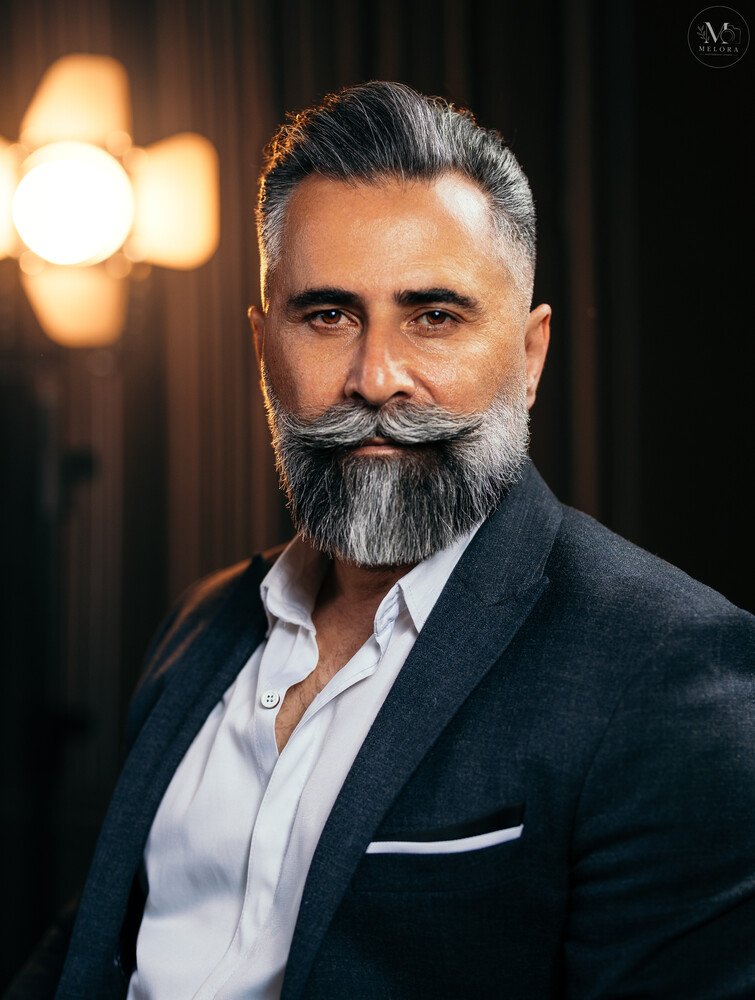 Portrait of a bearded man in dark blazer and white shirt against warm studio lighting
