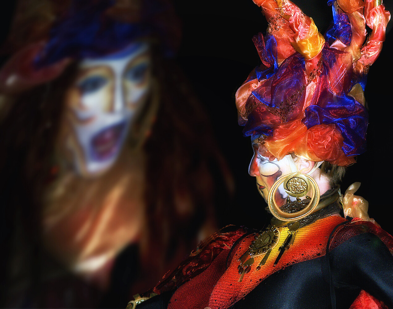 Performer in elaborate costume with flaming purple and orange headdress and ornate jewelry against dark background