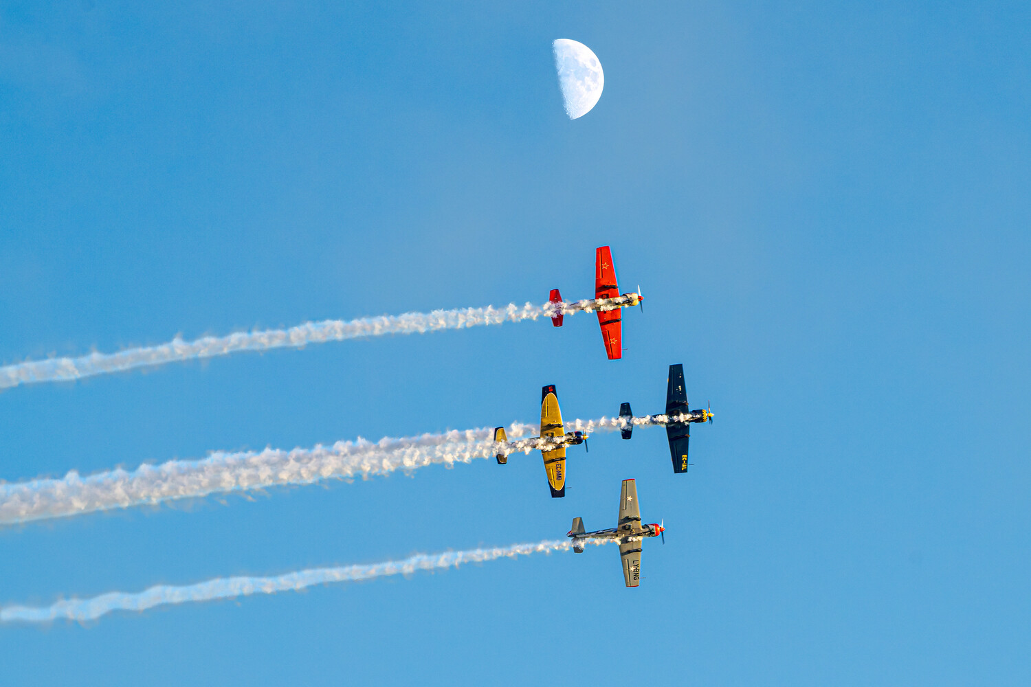 Formation of five aerobatic aircraft with smoke trails against blue sky and crescent moon
