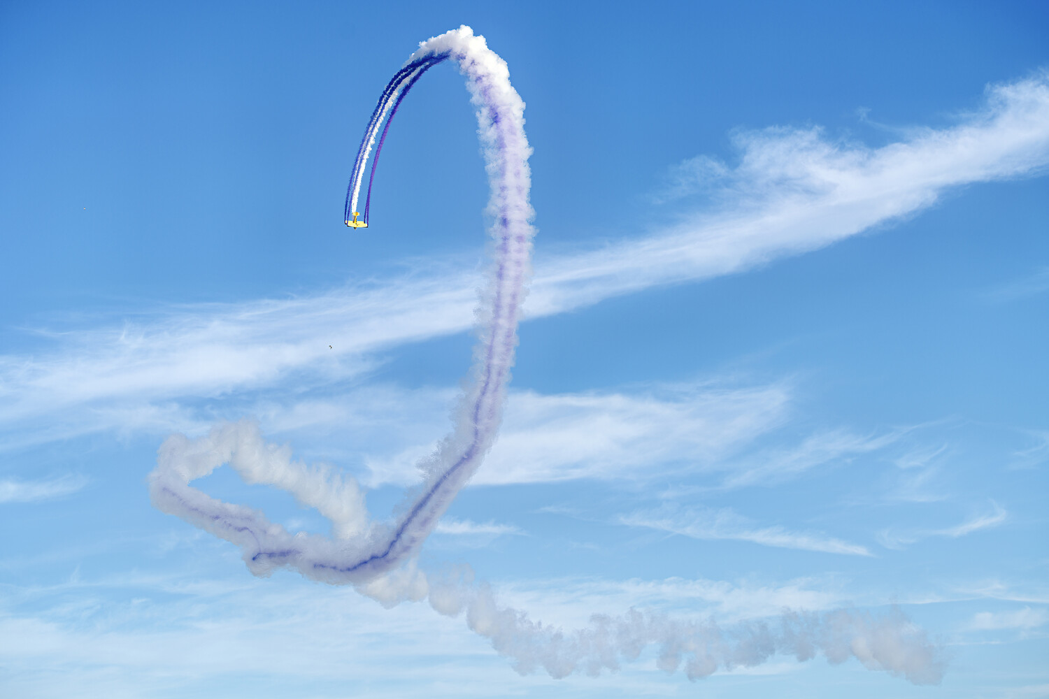 Stunt kite performing aerial maneuver with purple frame and white smoke trail against blue sky