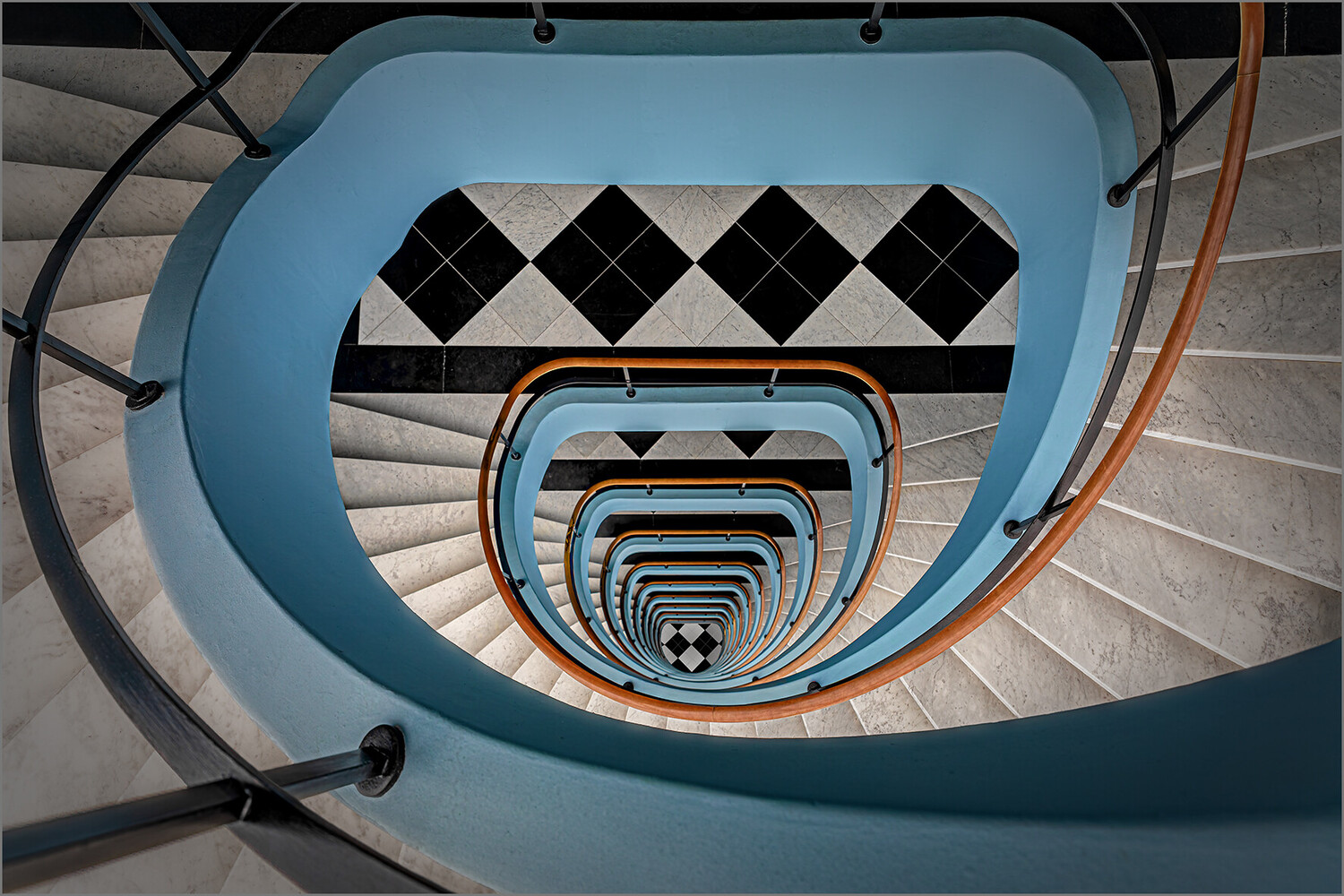 Spiral staircase shot from above with blue walls, orange railings, and geometric tile pattern at top