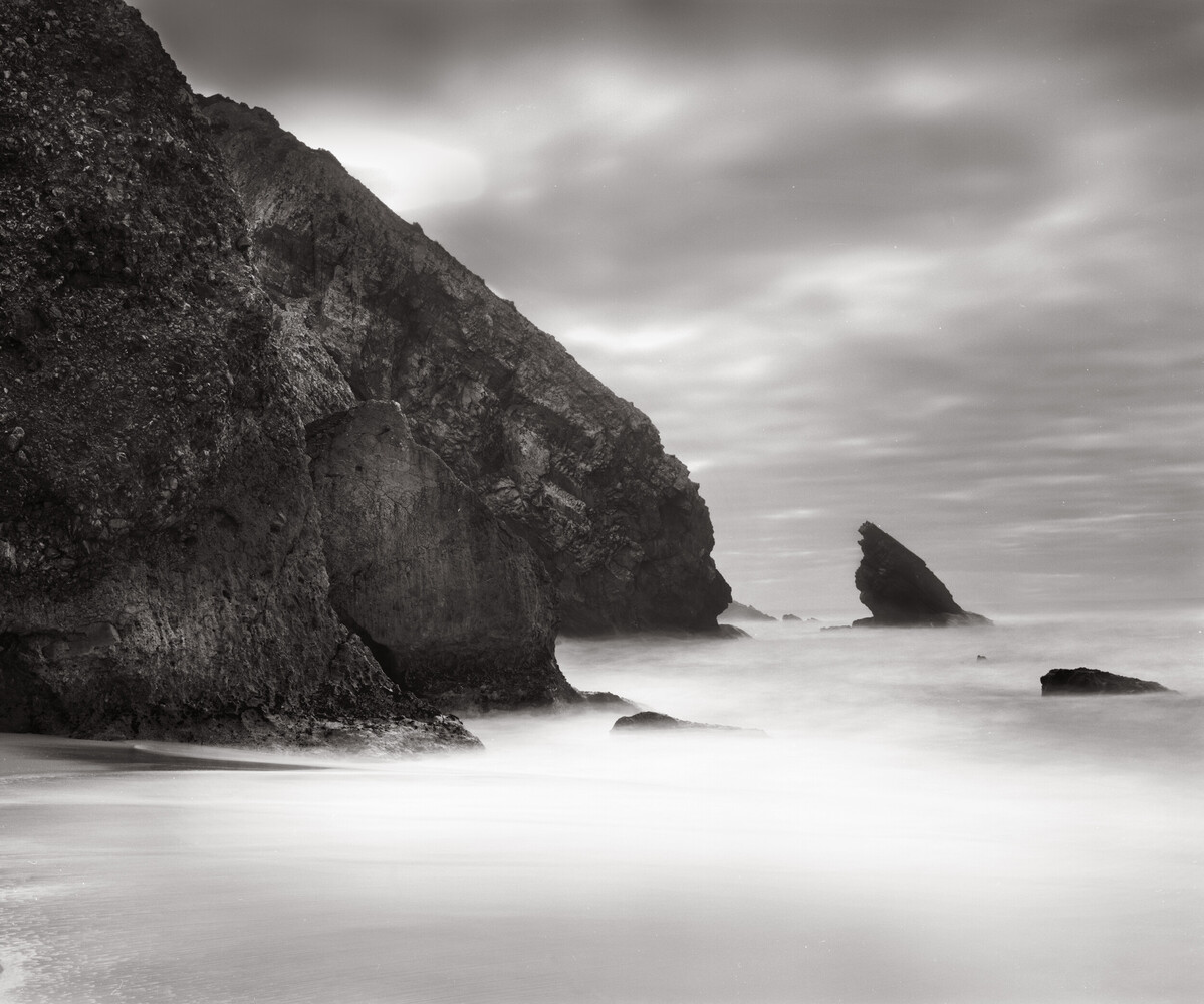 Rugged coastal cliffs and sea stacks with misty waves in black and white