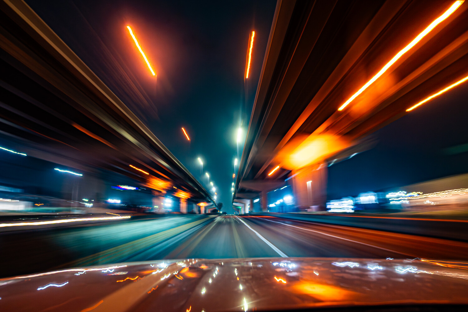 Highway shot taken from moving vehicle showing converging lanes with orange and blue light trails at night