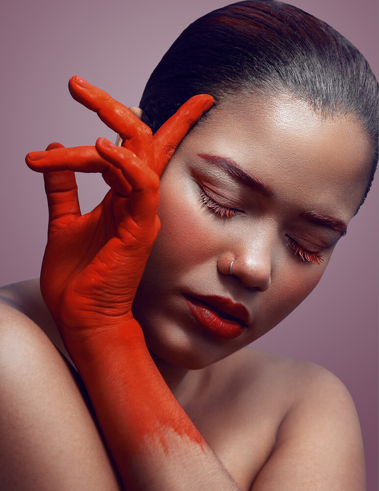 Woman with red paint on hand and face, eyes closed, against purple background