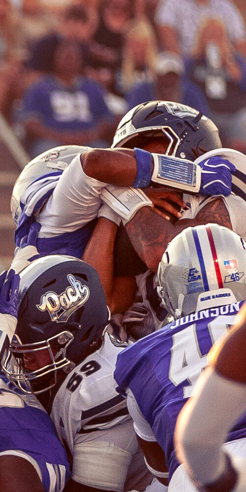 Football players in purple uniforms colliding during a tackle, captured mid-action with selective focus