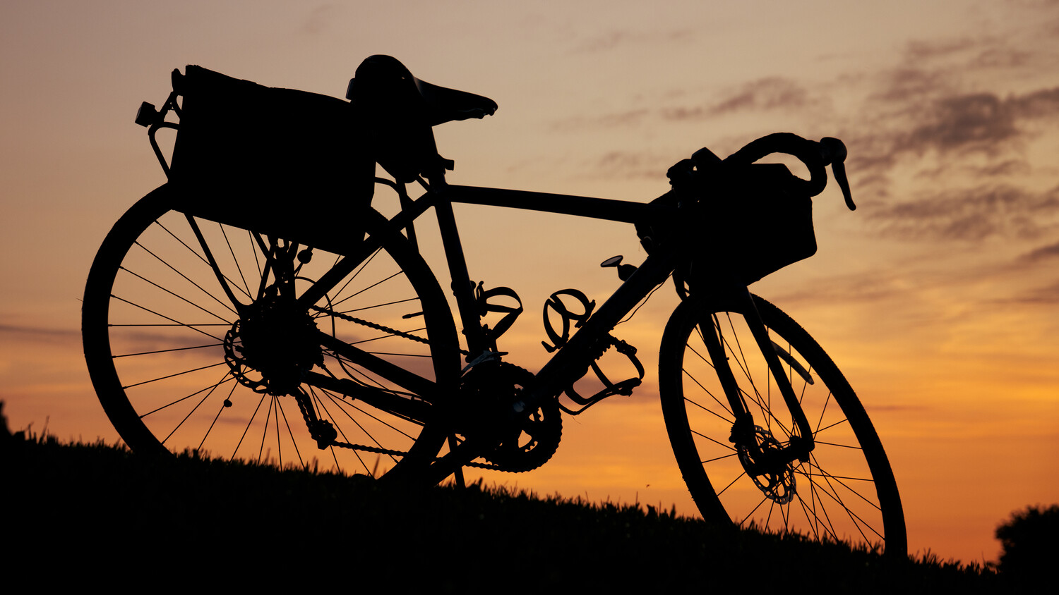 Silhouetted bicycle with front and rear pannier bags against golden sunset sky