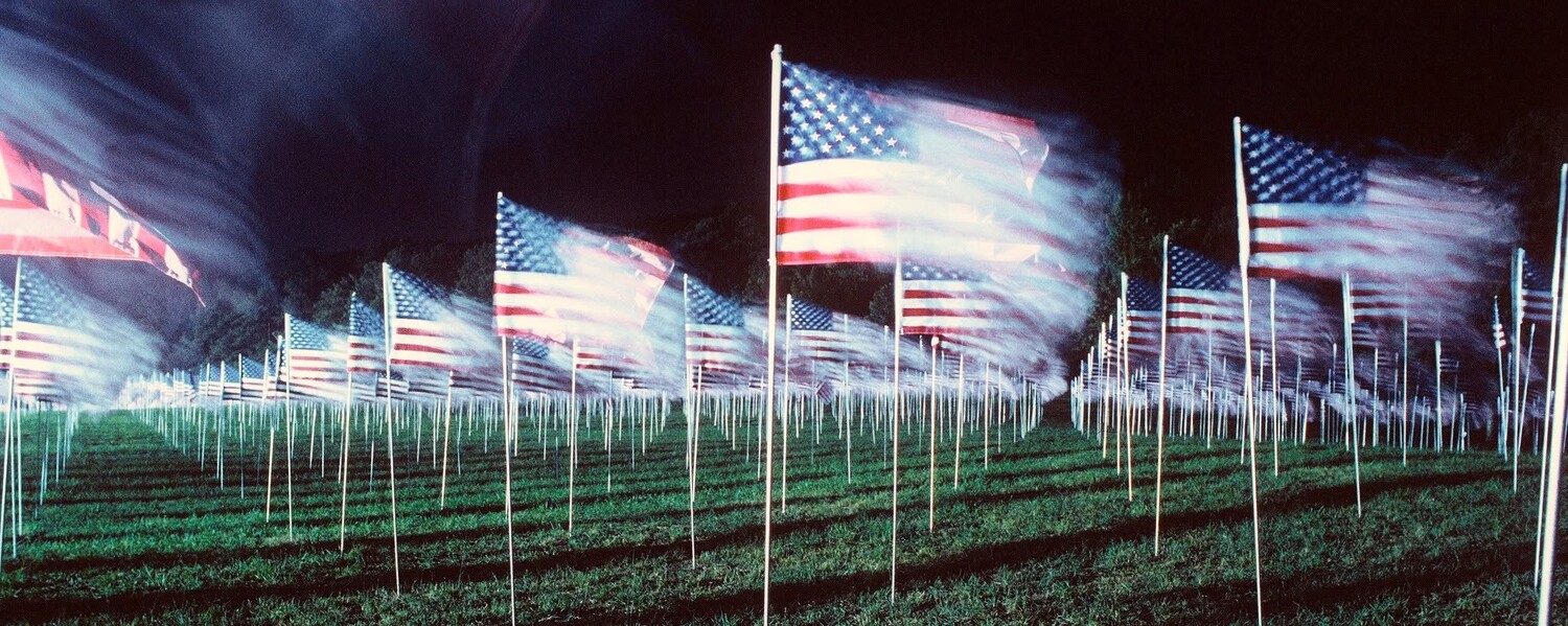 Field of American flags planted in rows with motion blur effect against dark sky