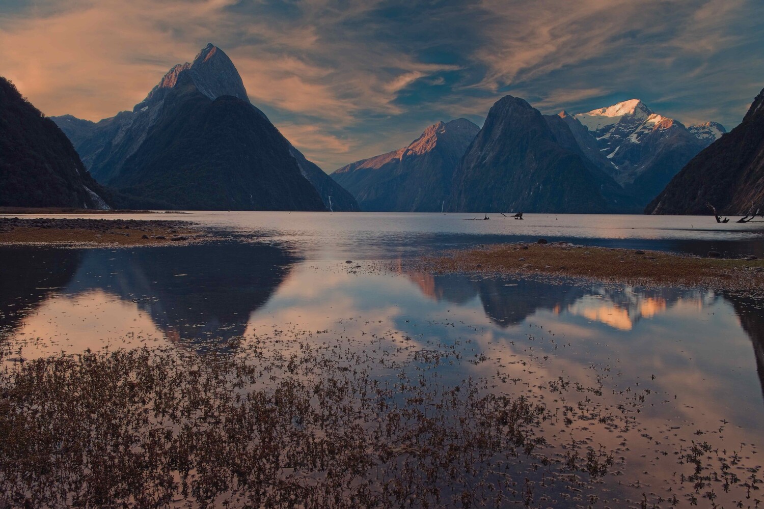 Dramatic fjord landscape with snow-capped peaks reflected in still water at golden hour