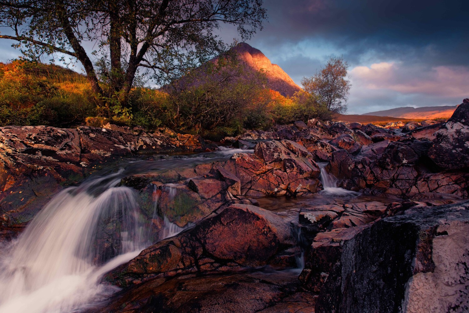 Waterfall cascading over rocky terrain with a cone-shaped mountain glowing in warm light at sunset