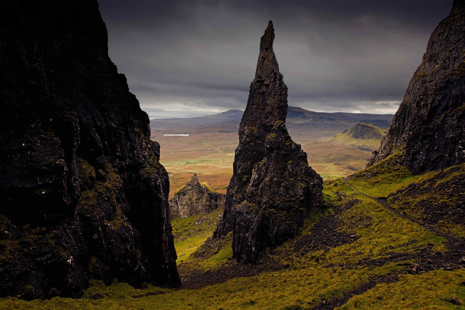 Dramatic rocky pinnacles frame a misty valley landscape beneath moody clouds