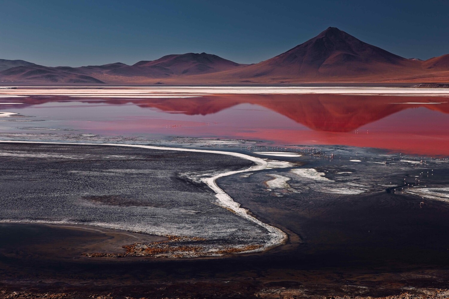Surreal landscape with pink salt lake reflecting cone volcano under clear sky