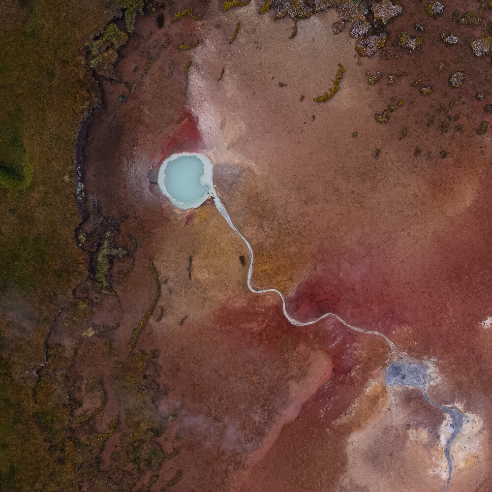 Aerial view of a turquoise pool and a pale winding path cutting through red-brown mineral-stained flats