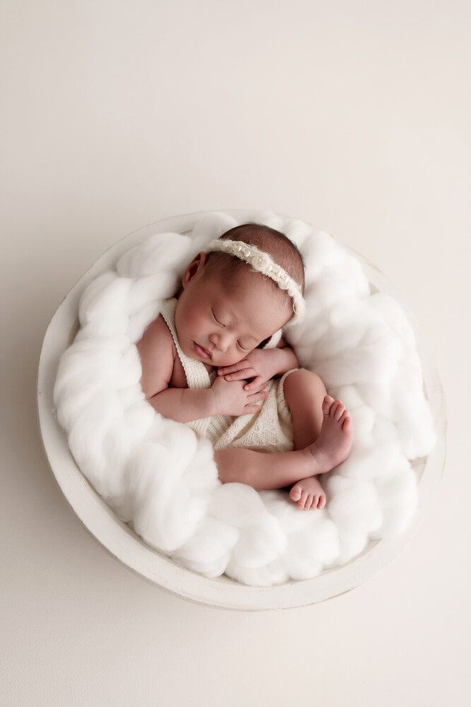 Sleeping newborn baby wrapped in white fabrics on a circular white posing pod