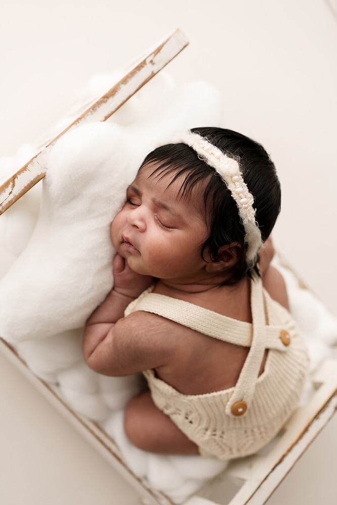 Newborn baby sleeping in cream-colored wrap with matching headband, overhead view