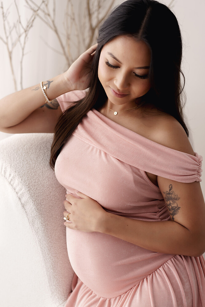 Pregnant woman in pink draped fabric cradling belly against neutral background