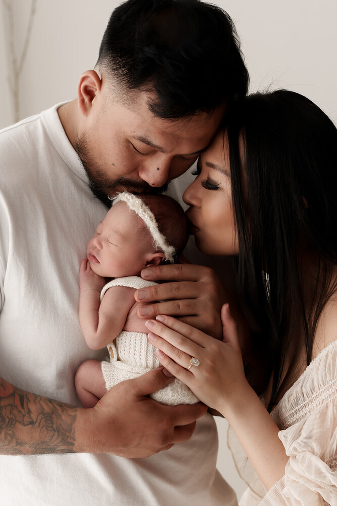 Parents holding and kissing their newborn infant in soft studio lighting