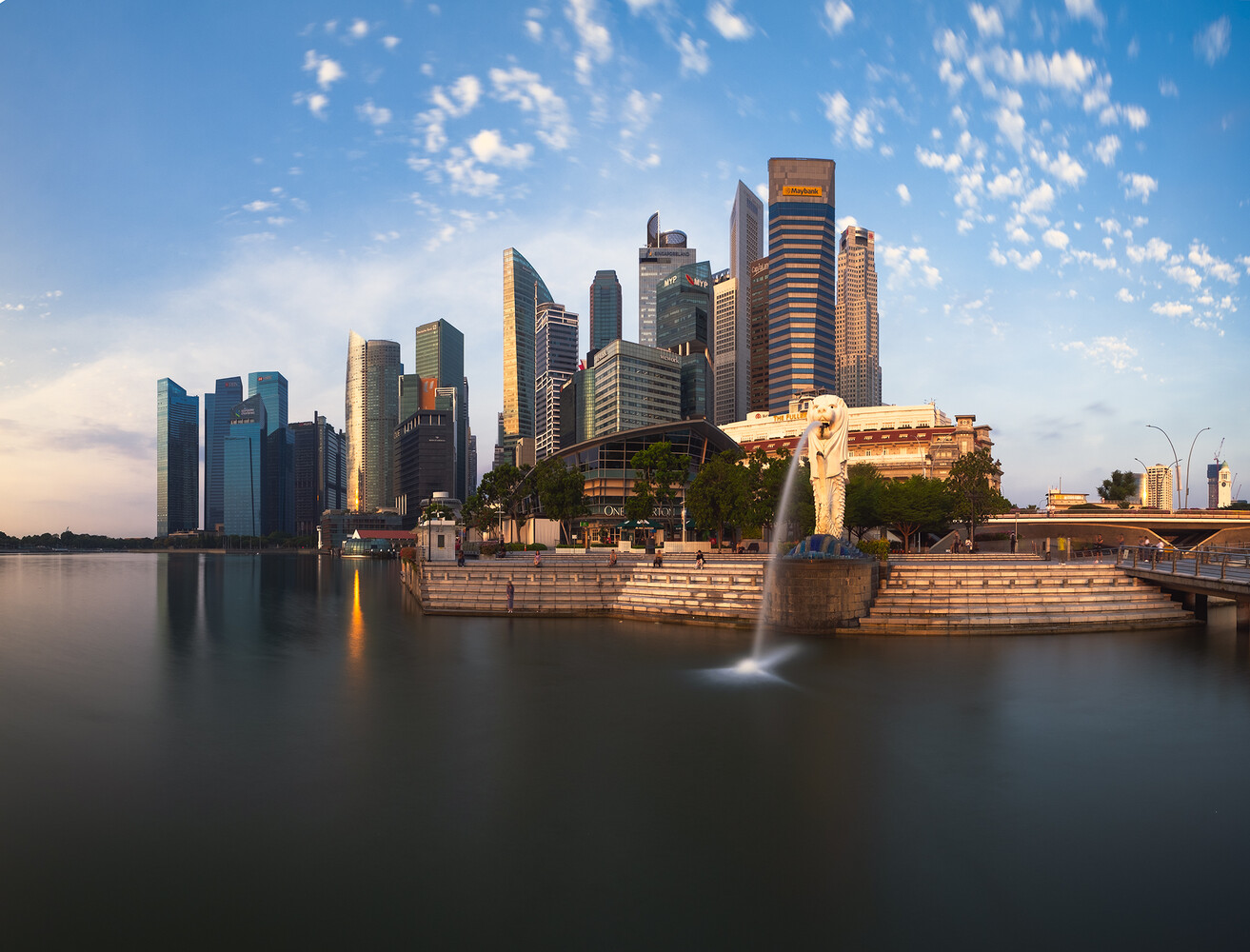 Merlion statue spouting water beside the Singapore skyline at dusk, with a smooth long-exposure bay in the foreground.