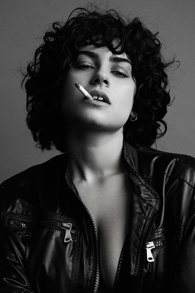 Black and white portrait of person with curly dark hair wearing leather jacket