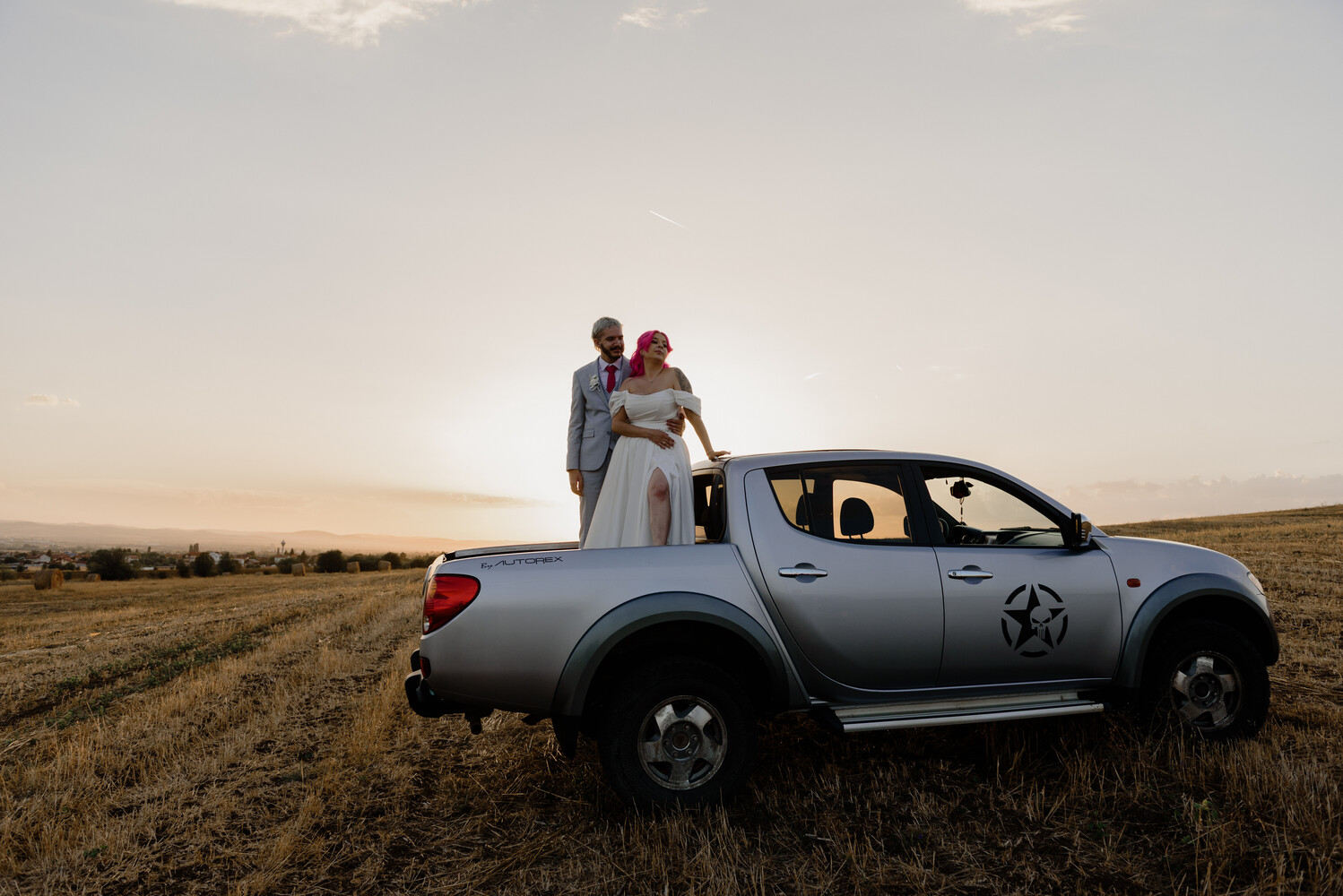 Couple standing on truck bed in open field at golden hour