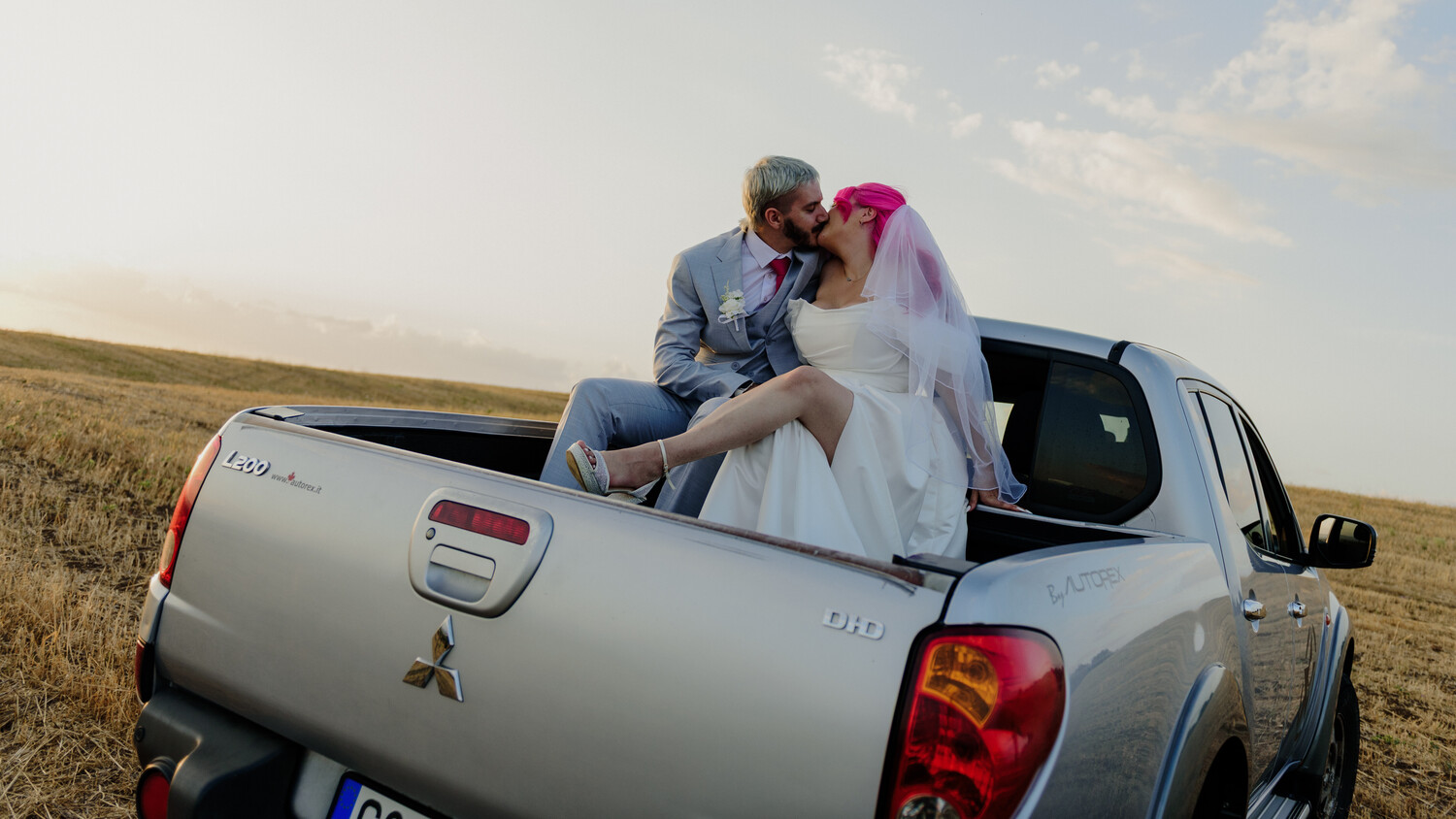 Couple kissing in truck bed during golden hour in open field
