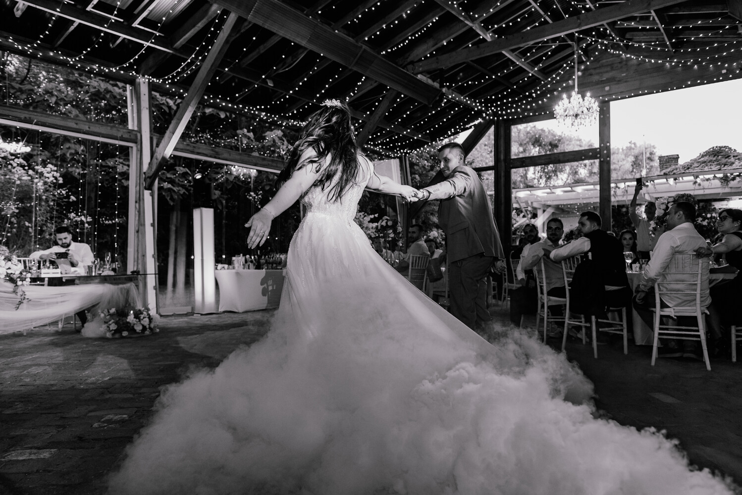 Bride in flowing white gown dancing under string lights at outdoor wedding reception